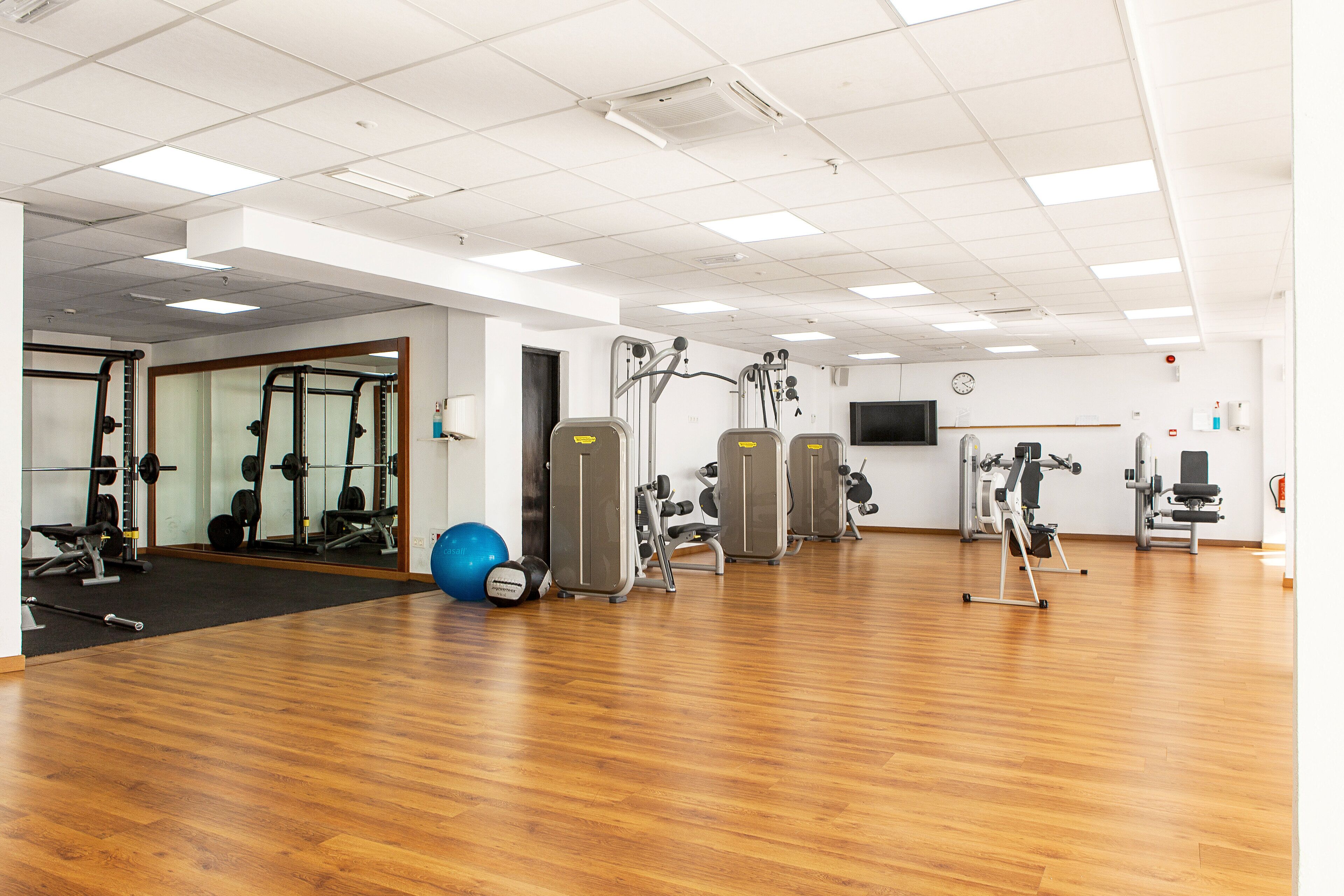 A spacious gym with various exercise machines, a blue exercise ball, and a wooden floor.