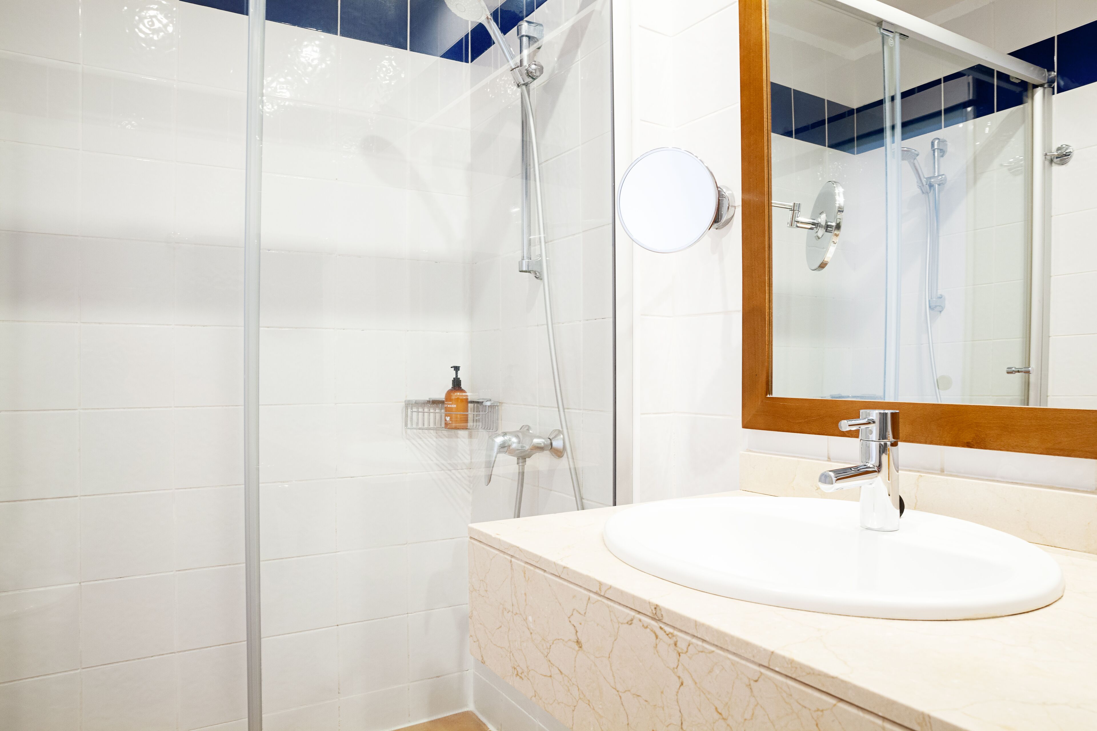 Un baño moderno con cabina de ducha de vidrio, un lavamanos blanco con encimera de mármol y un espejo con marco de madera.
