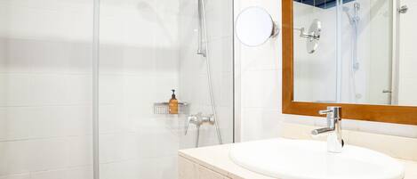 Un baño moderno con cabina de ducha de vidrio, un lavamanos blanco con encimera de mármol y un espejo con marco de madera.