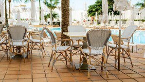 A poolside area with wicker chairs and tables, umbrellas, and palm trees. - Sunprime Atlantic View Suite & Spa (San Bartolomé de Tirajana)