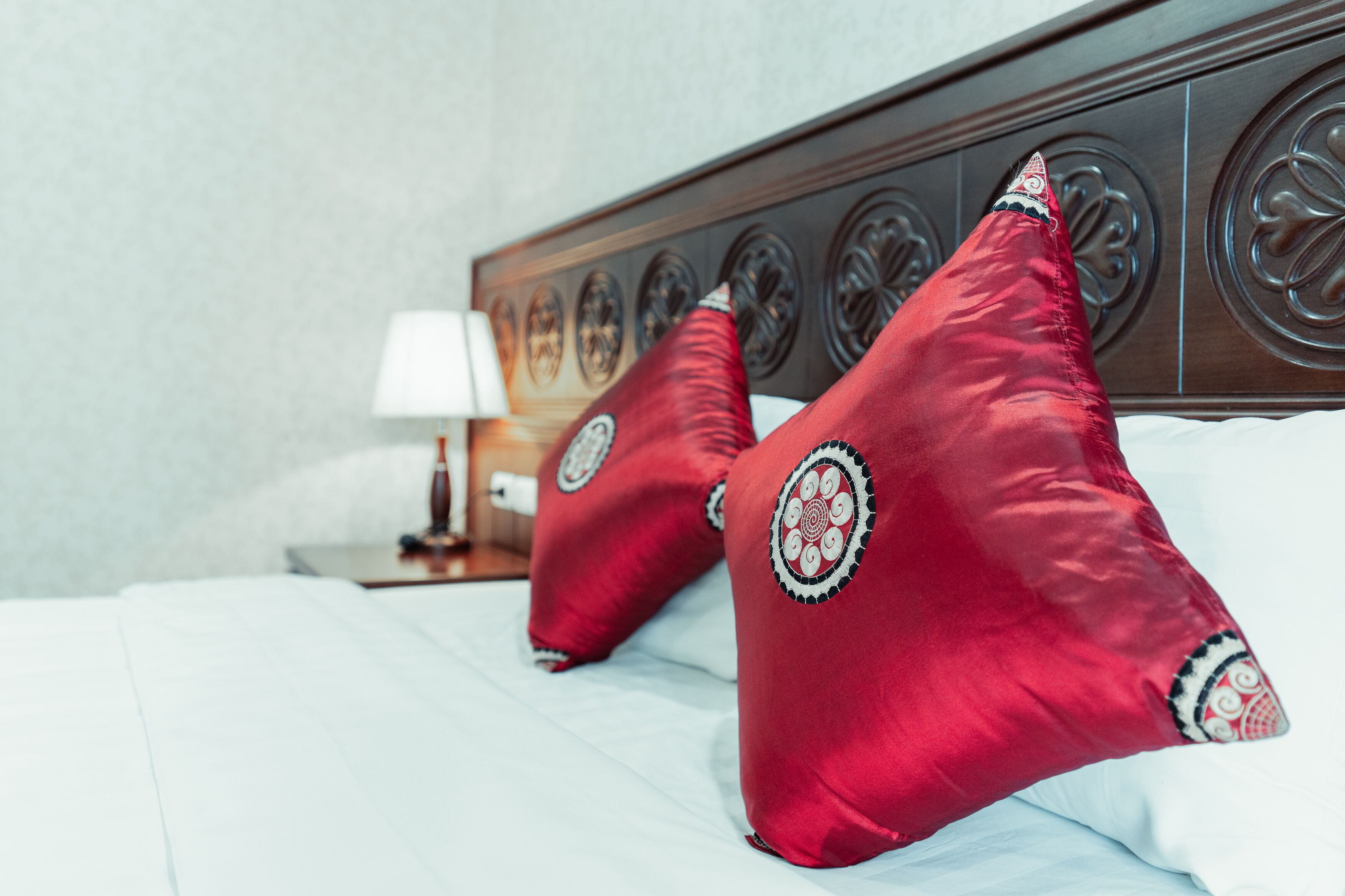 A bed with white bedding and two red pillows with circular patterns.