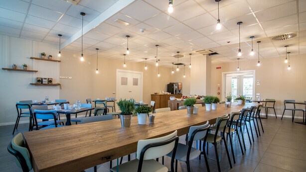 A spacious dining area with long wooden tables and chairs, potted plants, and pendant lighting. - Casa A Colori Padova (Padova)