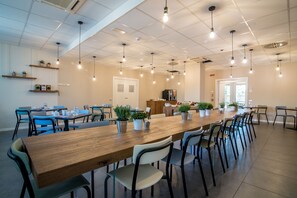 Un amplio comedor con largas mesas y sillas de madera, plantas en macetas e iluminación colgante.