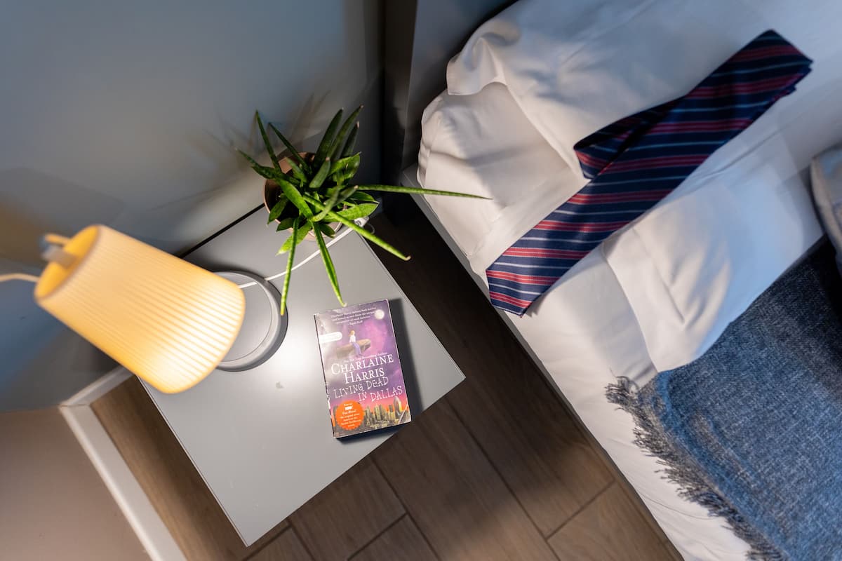 A bed with a striped tie, a book titled 'Living Dead in Dallas', and a lamp on a bedside table.