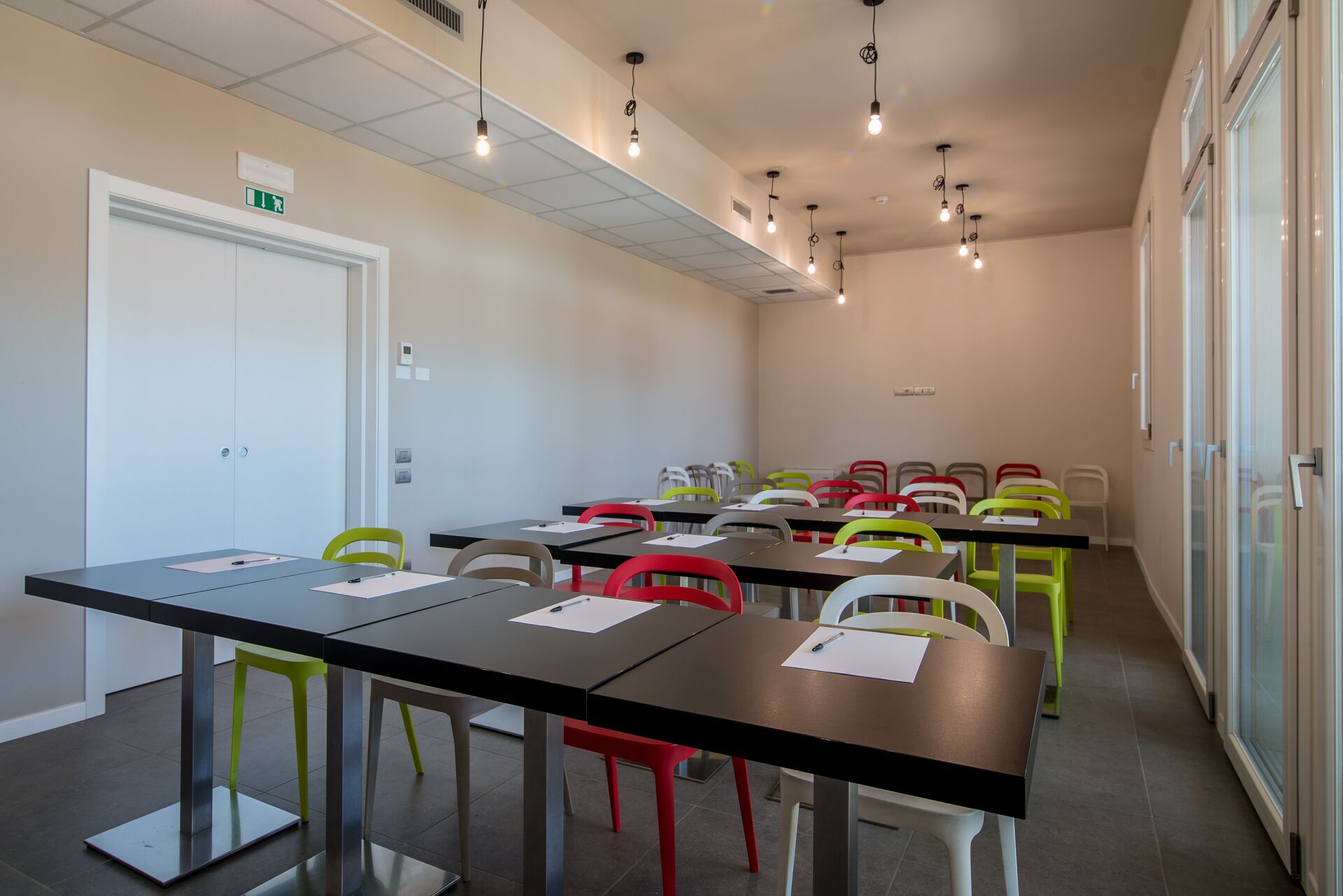 A conference room with tables and chairs, a white door, and a window with blinds.