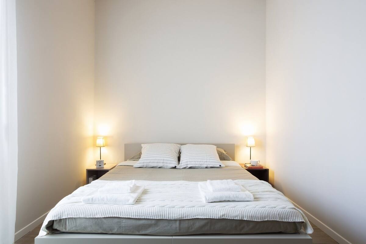 A neatly made bed with white linens and two bedside lamps.