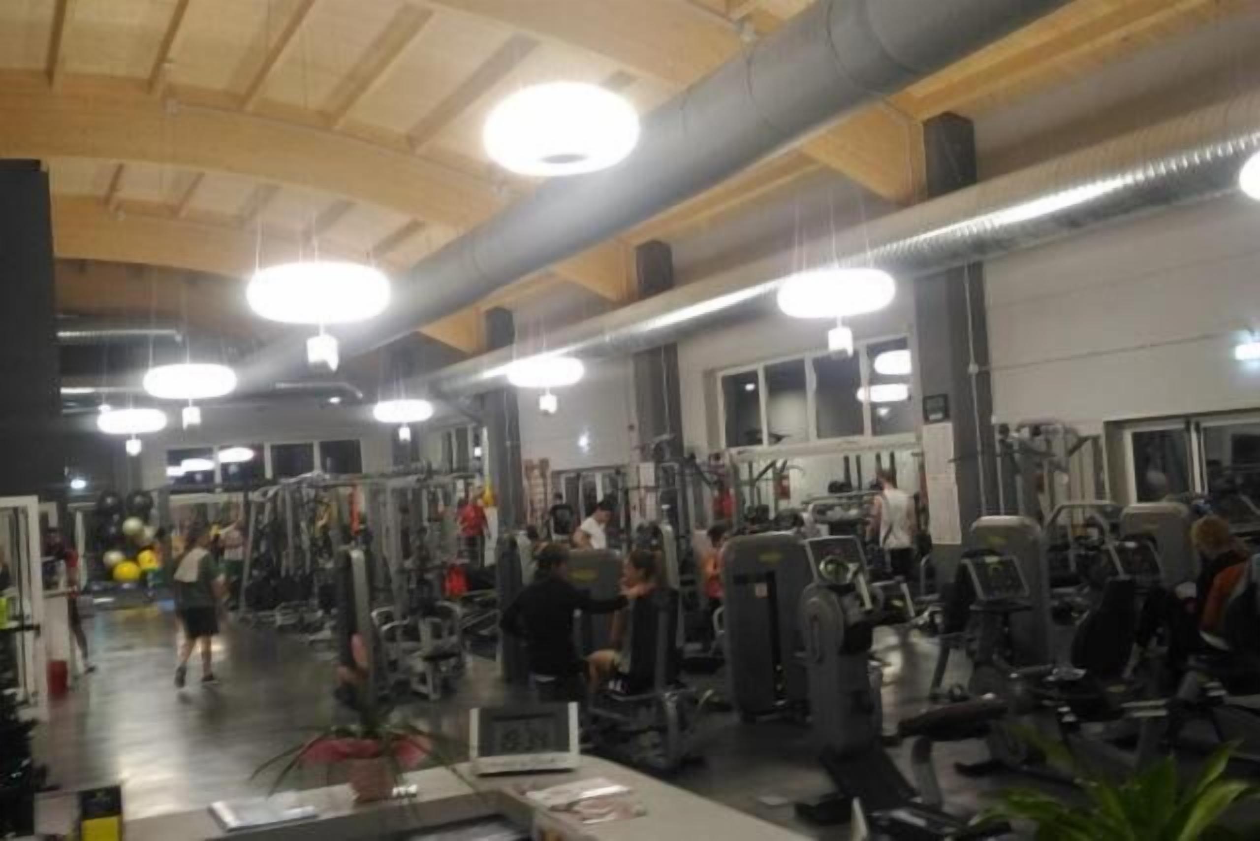 Un gimnasio con diversas máquinas de ejercicio y pesas, techos altos con vigas a la vista e iluminación brillante.