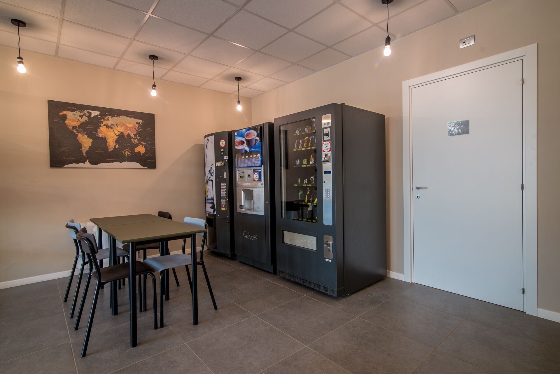 A small dining area with a table and chairs, two vending machines, and a door.