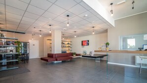 A spacious lobby with a red sofa, a reception desk, a vending machine, and a bookshelf. - Casa A Colori Padova (Padova)
