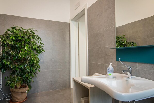 Un baño con una planta grande en maceta, un lavabo con dispensador de jabón y un espejo sobre el lavabo.