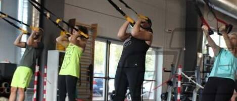 Un grupo de personas ejercitándose con correas de suspensión TRX en un gimnasio.