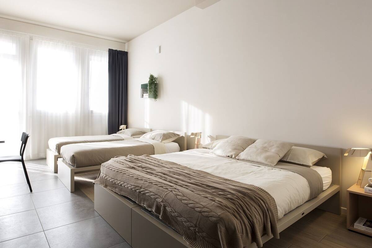 A modern bedroom with two beds, a chair, and a bedside table with a lamp.