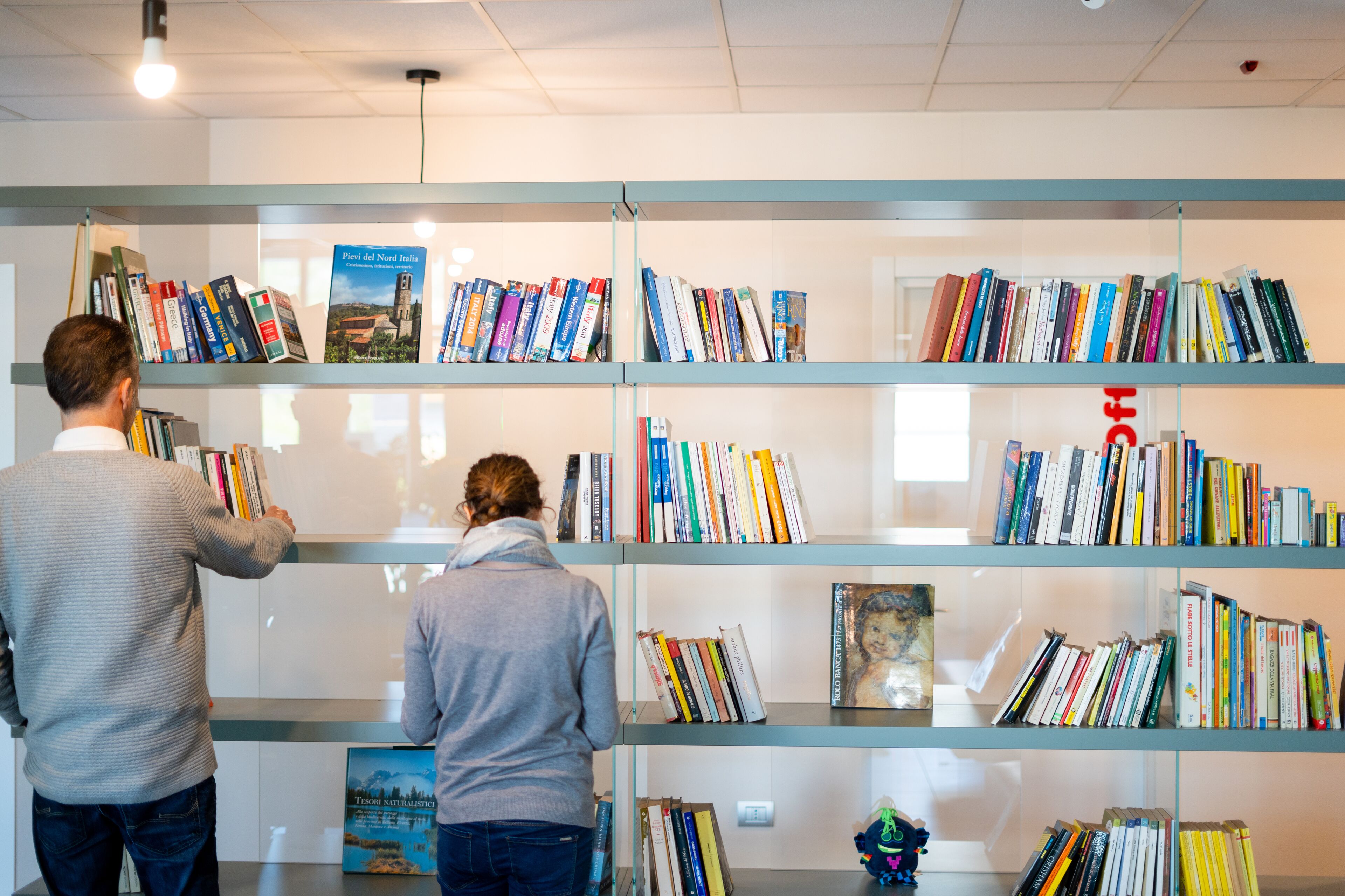 Deux personnes feuilletent des livres sur des étagères dans une bibliothèque.