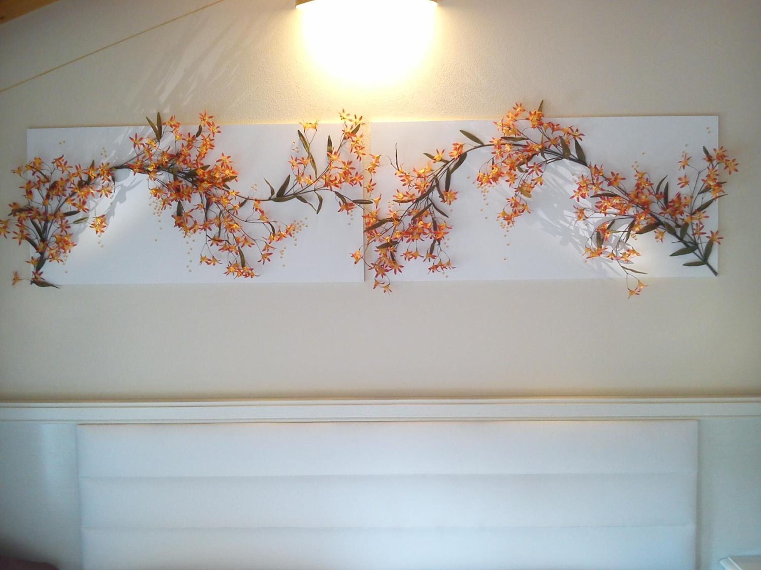 Ett väggmonterat konstverk med blommor och grenar.