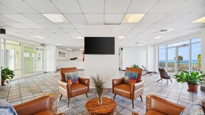 A spacious lobby with leather chairs, a wooden coffee table, and a large flat-screen TV mounted on the wall. - Holiday Terrace Beachfront Hotel, a By The Sea Resort (Panama City Beach)