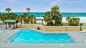 A swimming pool with a white fence, surrounded by palm trees and a beach in the background. - Holiday Terrace Beachfront Hotel, a By The Sea Resort (Panama City Beach)