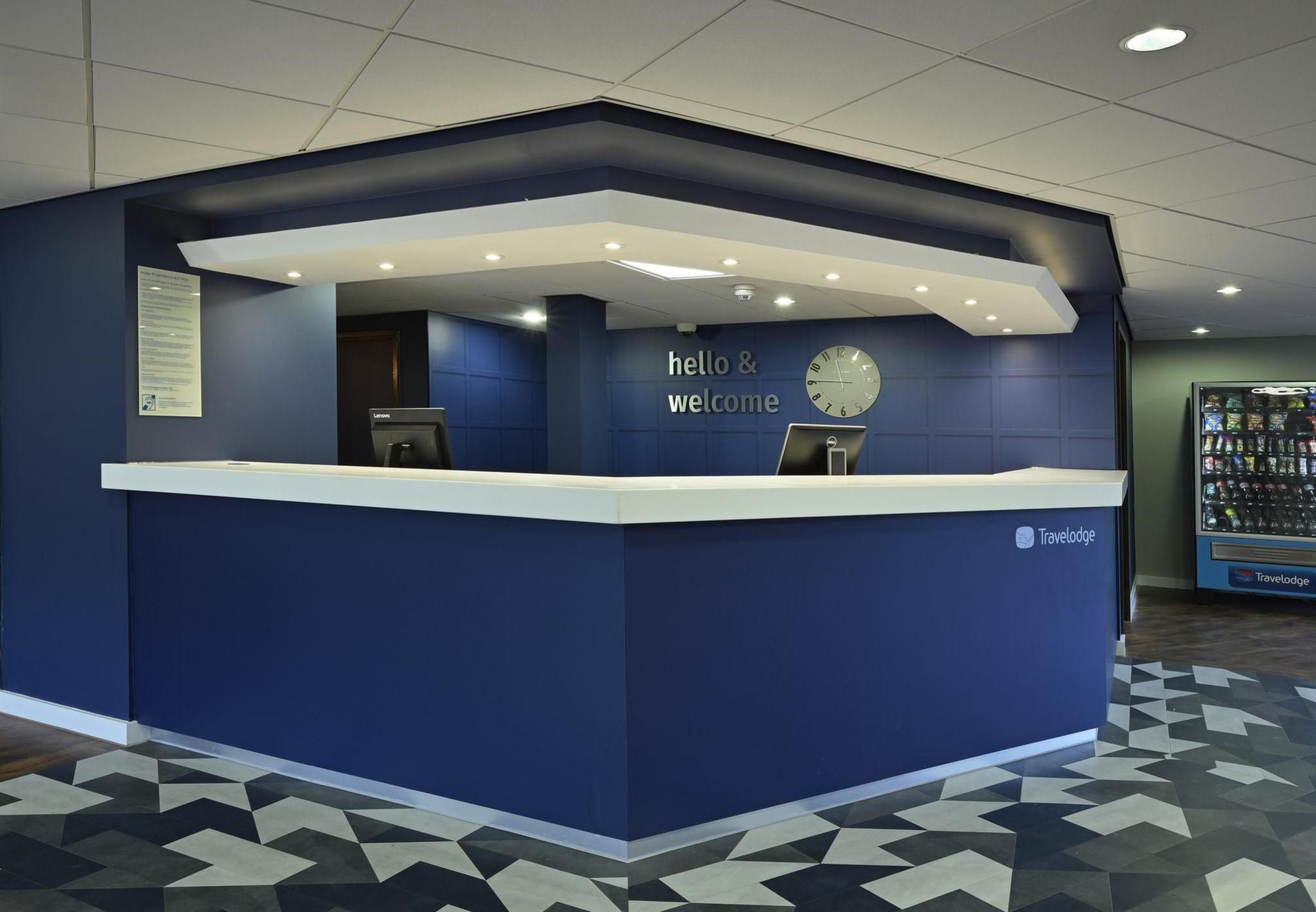 A reception desk with a 'hello & welcome' sign, a clock, and a Travelodge logo.