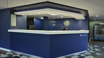 A reception desk with a 'hello & welcome' sign, a clock, and a Travelodge logo.
