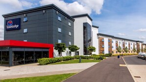 Un hôtel Travelodge au design moderne, reconnaissable à son enseigne Travelodge bien visible, à son auvent rouge et à son espace extérieur bien entretenu, avec un chemin pavé et des haies soigneusement taillées.