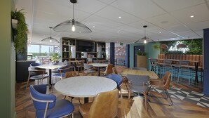 Un café moderne avec des tables rondes, des chaises bleues et marron, et un panneau néon indiquant « bar café ».