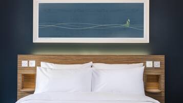 A neatly made bed with white linens, a framed artwork above it, and a wooden headboard with built-in lighting.