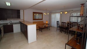 Un espace de vie compact comprenant un coin cuisine, un coin repas et un espace détente avec un canapé et des fauteuils.
