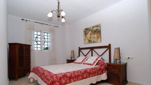 Une chambre à coucher comprenant un lit, une table de chevet, une armoire en bois, une fenêtre avec des rideaux et un tableau accroché au mur.
