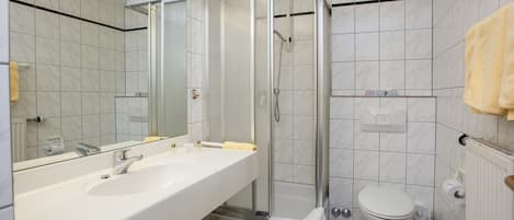 A bathroom with a white sink, mirror, shower enclosure, toilet, and towel rack.