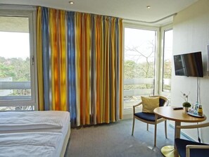 A hotel room with a bed, a chair, a small table with a plant, and a TV. - St.-Michaels-Heim Hotel (Berlin)