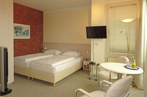Habitación de hotel con cama doble, televisor montado en la pared, mesita de noche con lámpara, una pequeña mesa con bandeja y una silla.