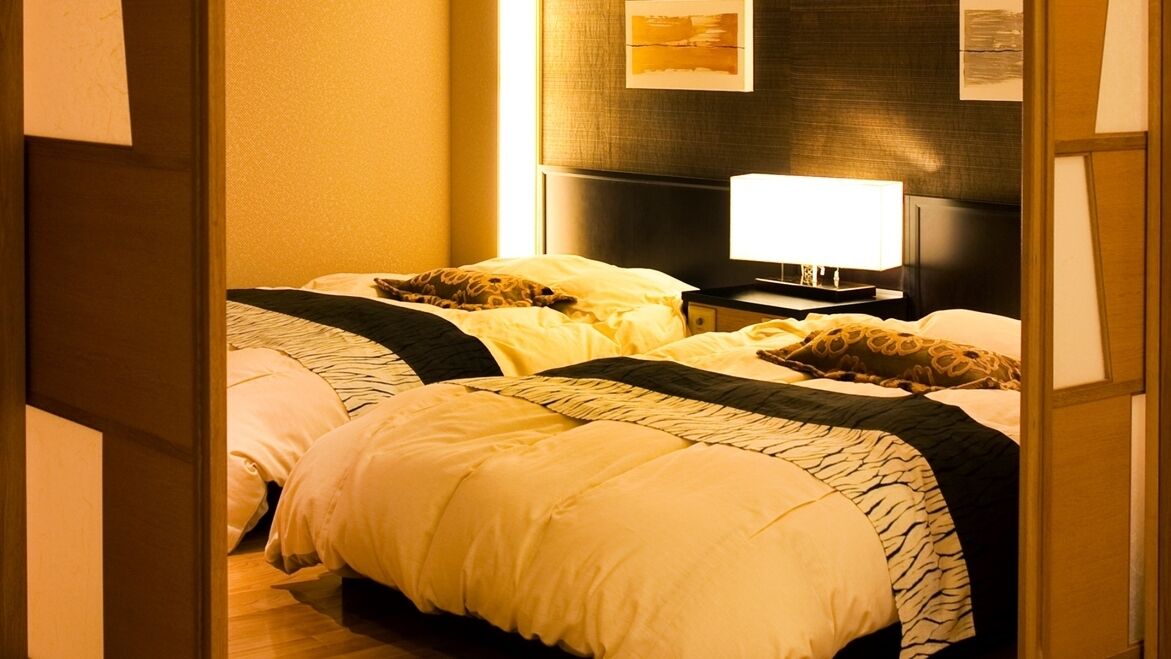 A hotel room with two beds, a television, and a wall-mounted lamp.