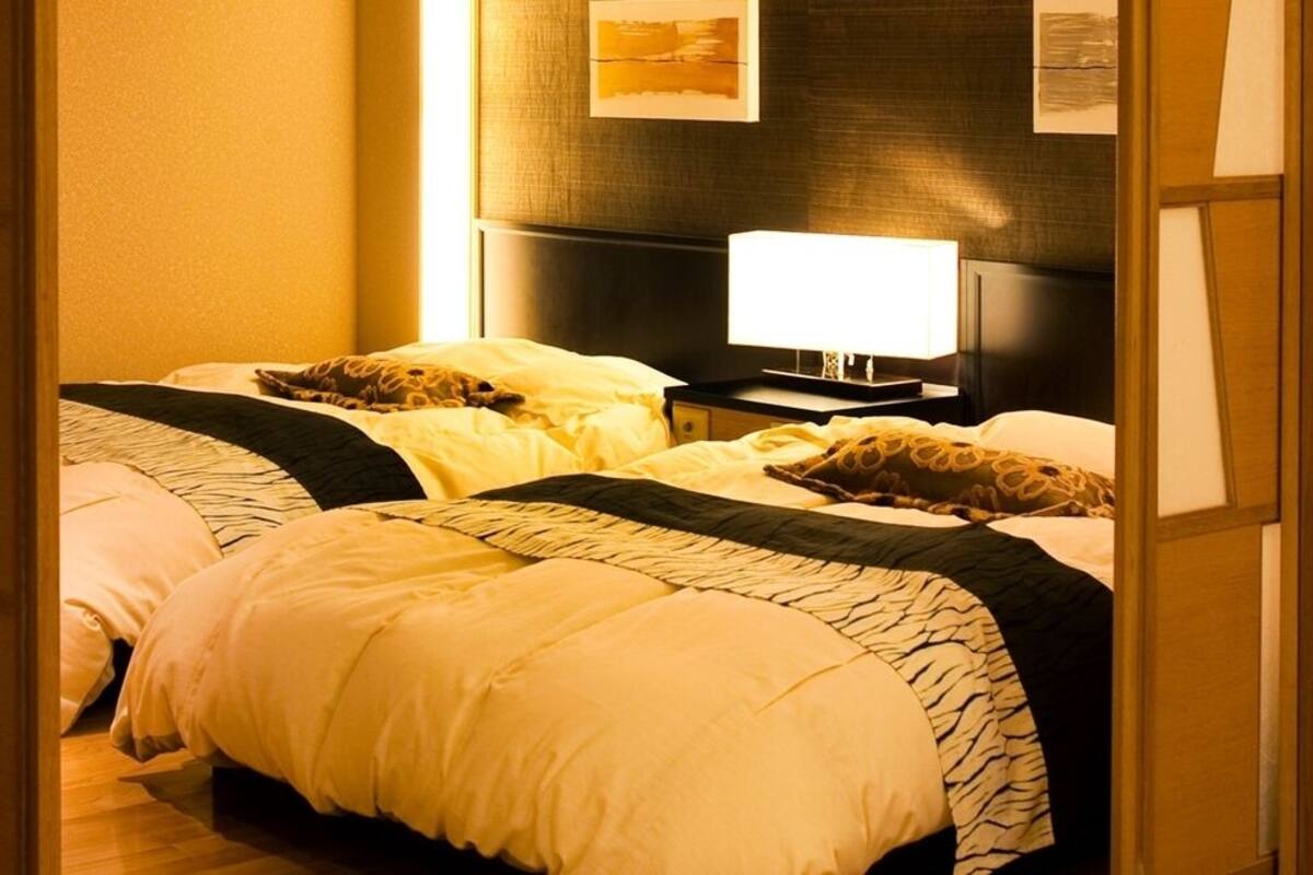 A hotel room with two beds, a television, and a wall-mounted lamp.