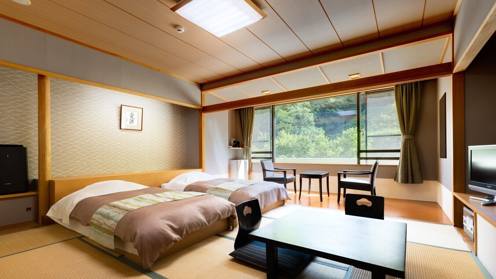 A hotel room with a bed, a desk, a chair, a television, and a view of greenery through the window.
