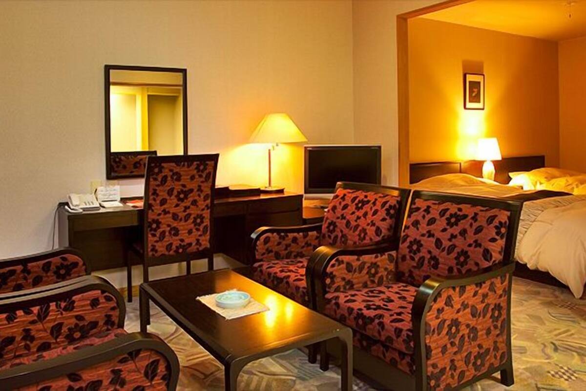 A hotel room with a desk, two chairs, a bed, a TV, and a lamp.
