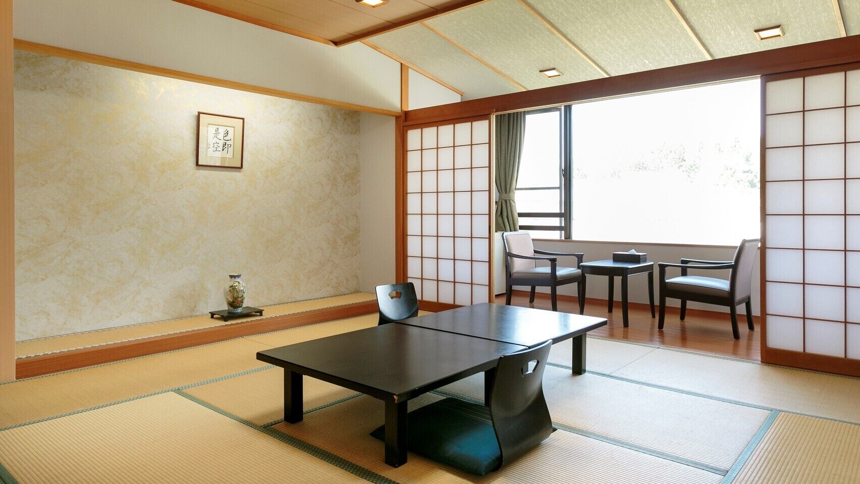A tatami mat room with a low table and chairs, a shoji screen, and a window with a view.