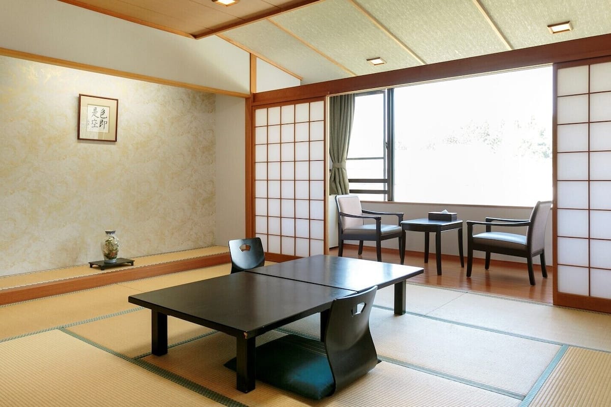 A tatami mat room with a low table and chairs, a shoji screen, and a window with a view.