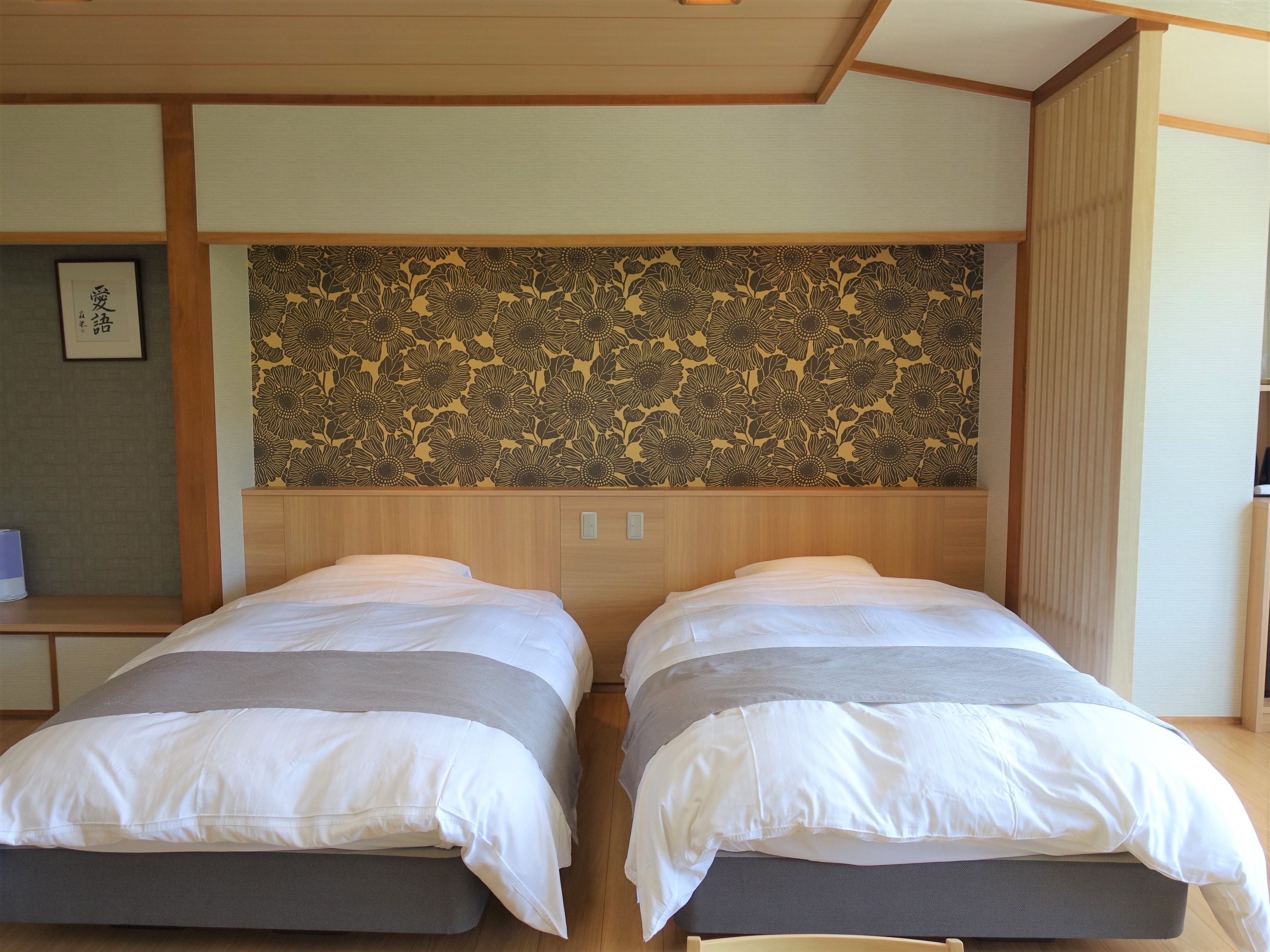 Une chambre avec deux lits, une tête de lit en bois et un papier peint à motifs floraux.