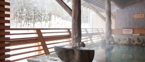 A traditional stone mortar in a wooden structure with a wooden railing and a stone wall with inscriptions.