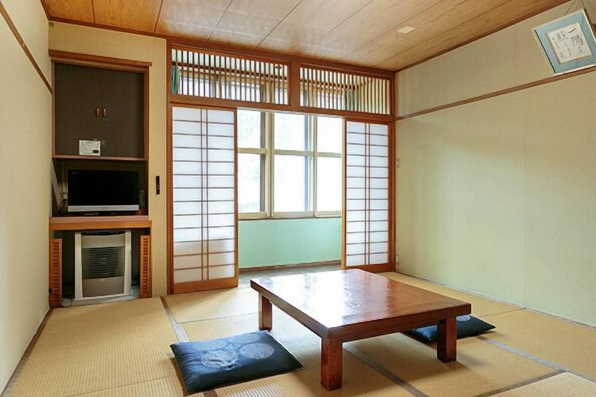A traditional Japanese room with tatami flooring, a low wooden table, sliding shoji doors, and a television on a shelf.