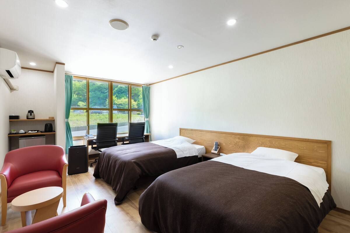 A hotel room with two beds, a desk, a chair, and a small table.
