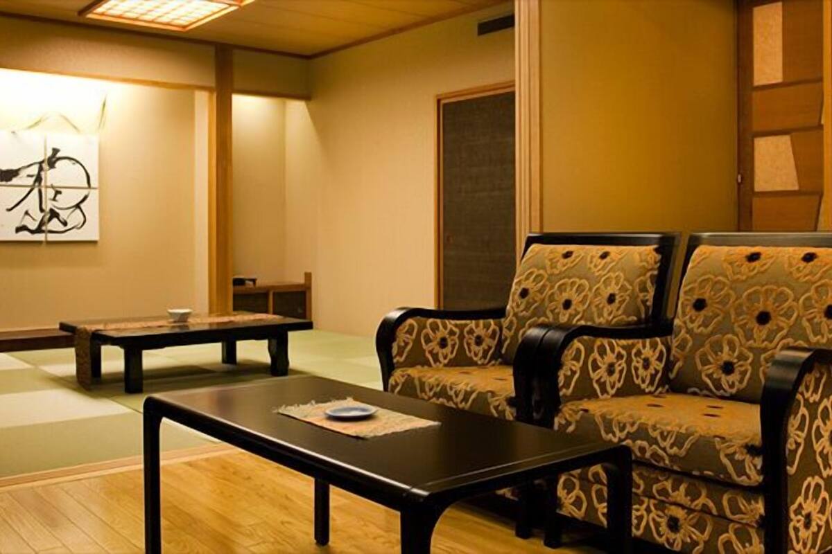 A traditional Japanese room with tatami flooring, a low table, a sofa with patterned cushions, and a wall with calligraphy.