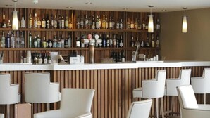 A bar area with a wooden wall and shelves of liquor bottles. There are white chairs and a white counter. - Park Central Hotel (Bournemouth)