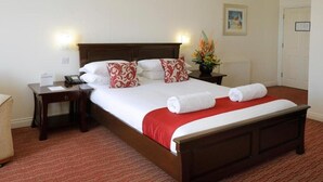 A neatly made bed with white and red linens, a wooden headboard, and two bedside tables with lamps. - Park Central Hotel (Bournemouth)