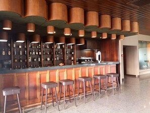 A bar area with a wooden bar counter and stools, overhead lighting, and a variety of bottles on shelves. - Estalagem Vianorte (Matosinhos)