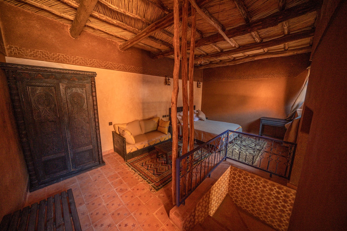 Habitación tradicional con puerta de madera, sofá, cama y escalera con barandilla de metal.