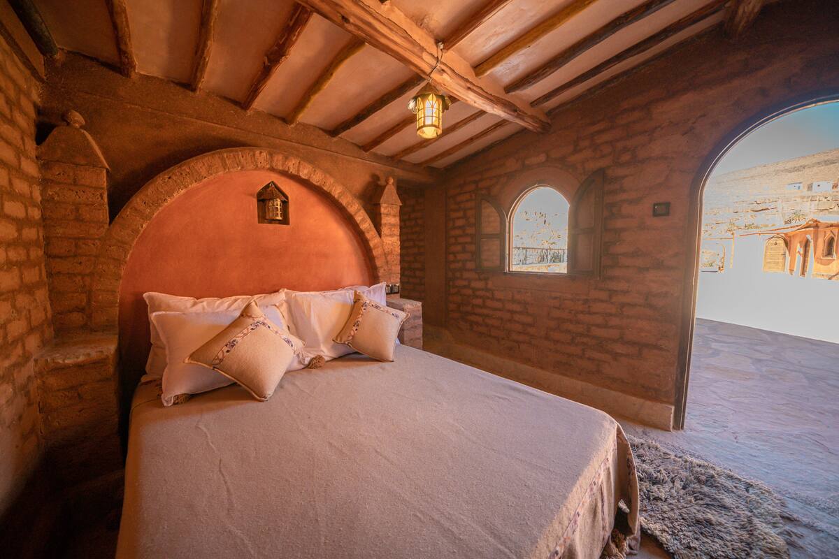 Un dormitorio con pared de piedra, techo de madera y cama con almohadas.