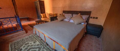Un dormitorio con una cama grande, una mesita de noche, un armario de madera y una alfombra estampada.