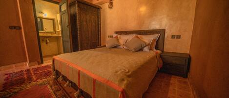 A bedroom with a large bed, a wooden wardrobe, and a bathroom visible through an open door.