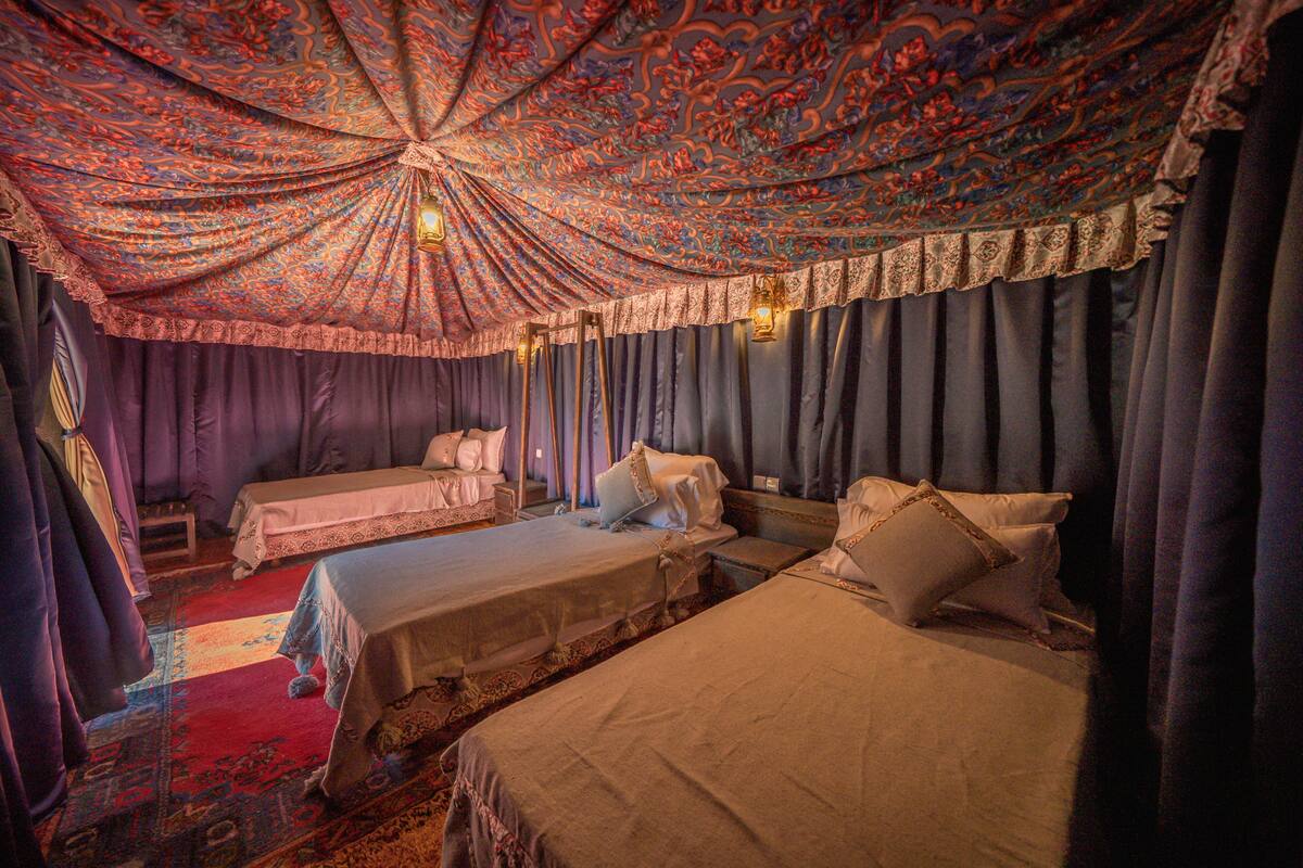 Una habitación con dos camas, un techo grande y ornamentado, y cortinas moradas.