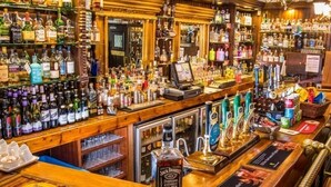 A bar area with a variety of liquor bottles, a cash register, and a Jack Daniel's whiskey bottle prominently displayed. - The Old Bell Inn (Oldham)
